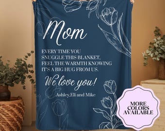 May include: A navy blue blanket with white floral illustrations and the word "Mom" in cursive. The blanket has a message that reads "Every time you snuggle this blanket, feel the warmth knowing it's a big hug from us. We love you!"