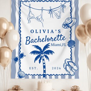 May include: A white and blue beach-themed banner with the text "OLIVIA'S Bachelorette Miami, FL EST. 2026". The banner features illustrations of a bikini, hat, sunglasses, palm tree, seashells, and flip-flops. Gold and white balloons are in the background.