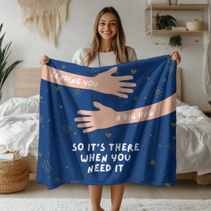 May include: Blue fleece blanket with a pink hand drawn illustration of two arms hugging. The text on the blanket reads "Sending you a big hug so it's there when you need it."