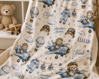 May include: A cream-colored fleece blanket featuring a repeating pattern of teddy bears in blue airplanes, hot air balloons, clouds, stars, and baby clothes. The text "Elijah," "Little Pilot," and "Adventure Awaits" is printed throughout the design.