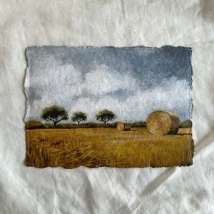 May include: A painting depicting a field with three trees and hay bales. The sky is a light blue with white clouds. The field is a golden yellow colour.