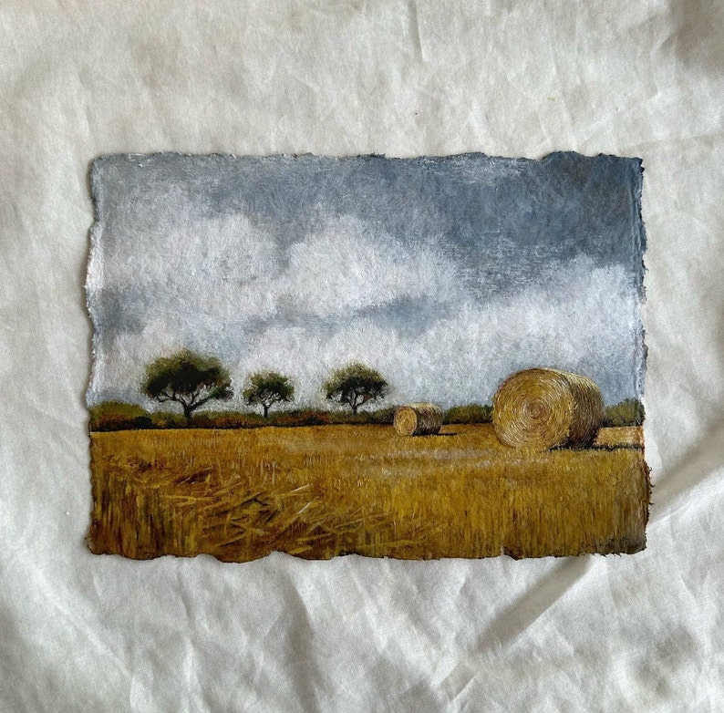 May include: A painting depicting a field with three trees and hay bales. The sky is a light blue with white clouds. The field is a golden yellow colour.