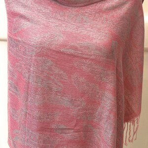 May include: A pink and silver patterned shawl with fringe on the edges.