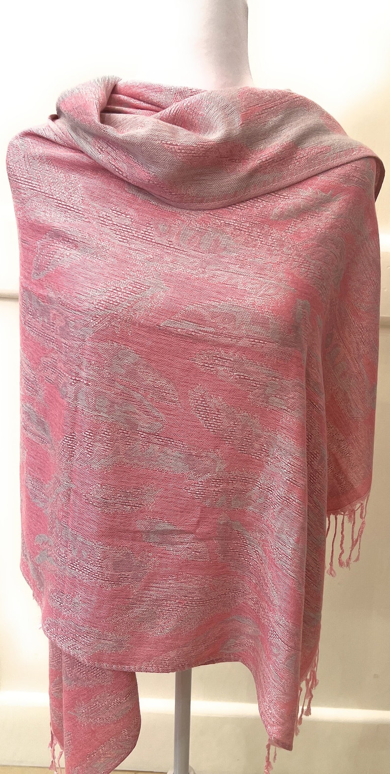 May include: A pink and silver patterned shawl with fringe on the edges.