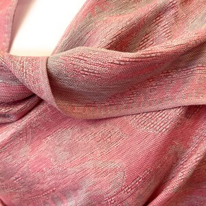 May include: A pink and silver patterned shawl made of a soft, woven fabric. The shawl is draped over a mannequin's shoulders.
