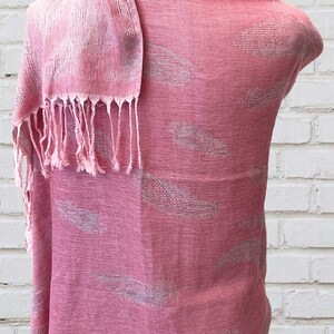 May include: A pink scarf with a white feather pattern. The scarf has a fringe on the bottom and is draped over a white mannequin.