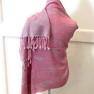 May include: A pink scarf with a white feather pattern and fringe. The scarf is draped over a white mannequin.
