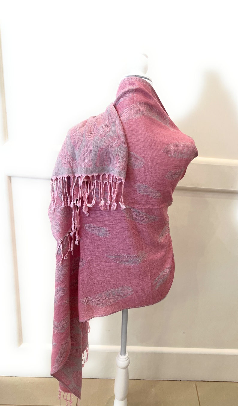 May include: A pink scarf with a white feather pattern and fringe. The scarf is draped over a white mannequin.