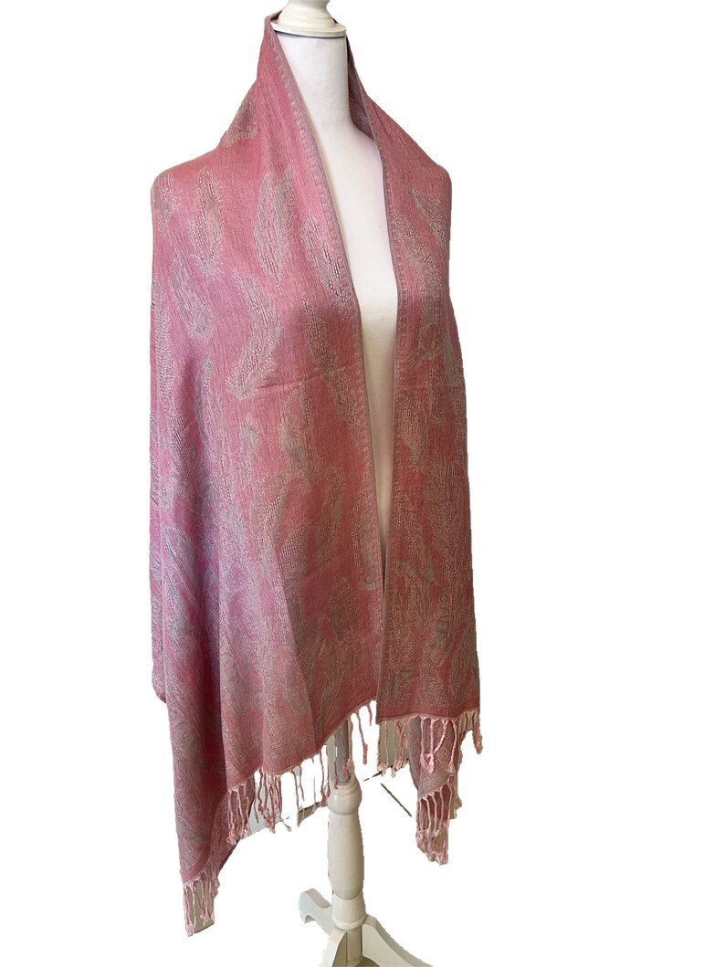 May include: A pink shawl with a white paisley pattern and fringe trim.