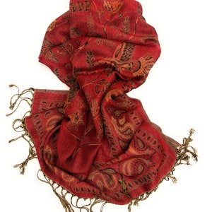 May include: A red scarf with an intricate paisley and floral pattern. The scarf has a fringe trim and is made of a soft, flowing fabric. The design includes shades of gold and black.