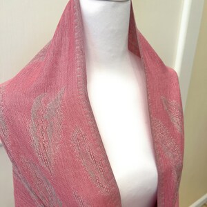 May include: A pink scarf with a white pattern. The scarf is draped over a white mannequin.