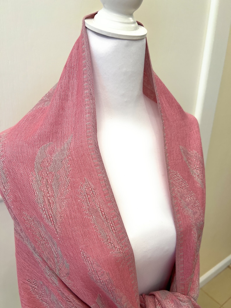 May include: A pink scarf with a white pattern. The scarf is draped over a white mannequin.