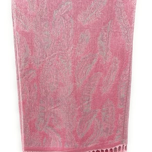 May include: A pink towel with a silver floral pattern and fringe trim.