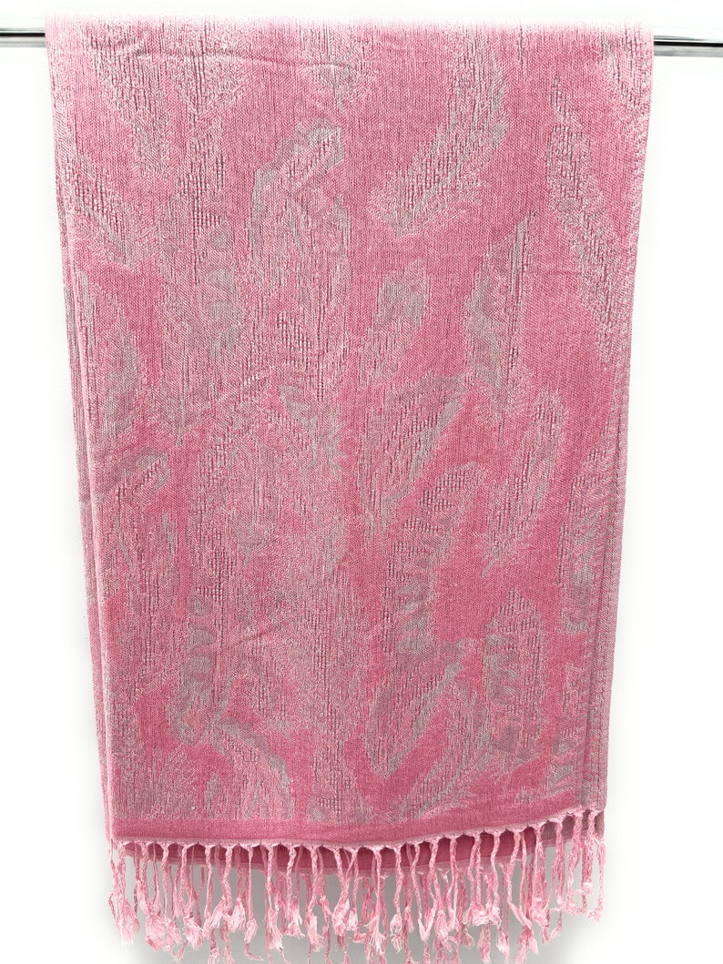 May include: A pink towel with a silver floral pattern and fringe trim.