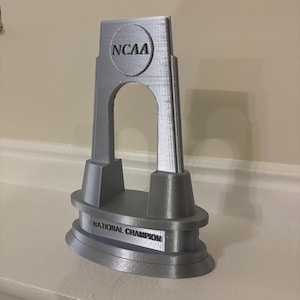 May include: A silver 3D printed trophy shaped like the NCAA arch with the words "NCAA" and "National Champion" on it.