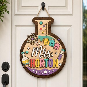 May include: A wooden door sign shaped like a laboratory flask, featuring the text Mrs. HORTON in colorful letters. The design includes an atom symbol, periodic table elements Co, N, and Sc, a test tube, and a beaker with yellow liquid.