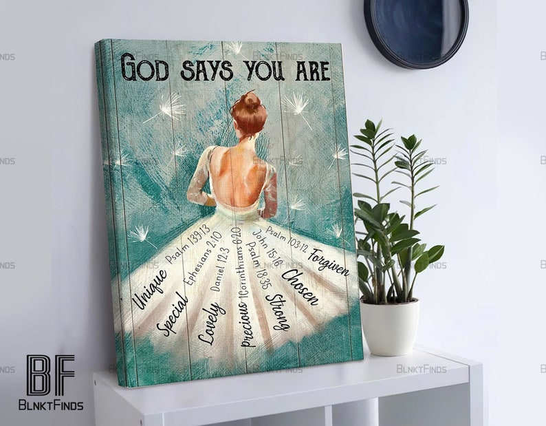May include: A teal and white canvas print with a woman in a white dress and the words "God Says You Are" at the top. The dress has words and bible verses printed on it, including "Unique", "Special", "Lovely", "Precious", "Forgiven", "Chosen", and "Strong".
