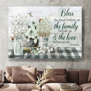 May include: A white wood sign with a green checkered background and a floral arrangement. The sign has a green inscription that reads "Bless the food before us the family beside us & the love between us Amen."