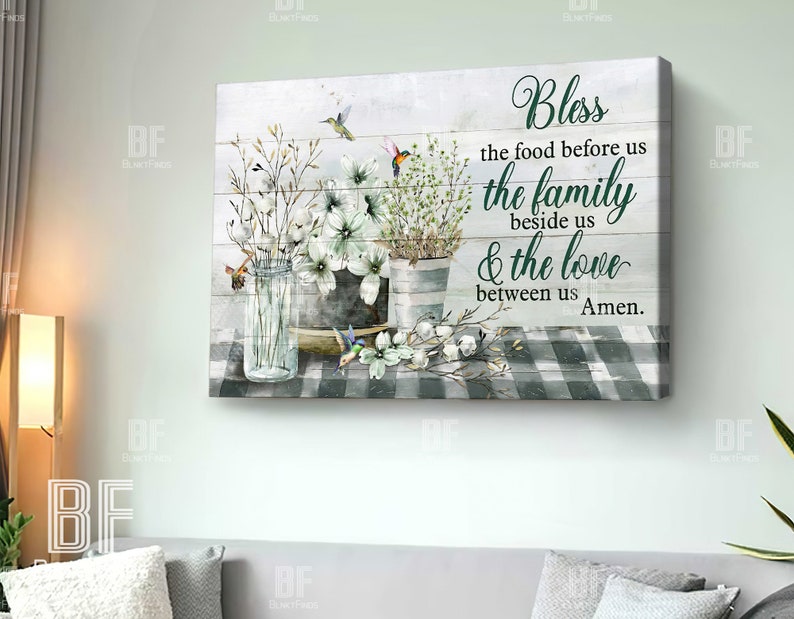 May include: A watercolor painting on a wood background with a white and green checkered tablecloth. The painting features a bouquet of white flowers in a glass jar, a metal bucket, and two hummingbirds. The text reads "Bless the food before us the family beside us & the love between us Amen."