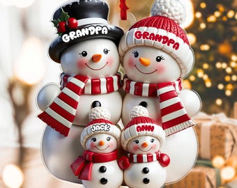 May include: A family of snowmen Christmas ornament. The snowmen wear red and white striped scarves and hats. The top snowmen are labeled "Grandpa", and the bottom snowmen are labeled "Jack" and "Ann". The ornament hangs from a red ribbon.