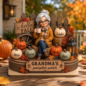 May include: A decorative figurine of a grandmother figure sitting on hay bales in front of a wooden fence. The display features pumpkins labeled with names Layla, Ethan, Mila, Lucas, Noah, and Ava, a lantern, and signs reading hello FALL and GRANDMA'S pumpkin patch.