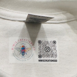 May include: A white t-shirt with a label featuring a bee logo and the text "Mimi's Creations Est. 2023 Personalised Designs" and a QR code with the text "mimiscreationsSD".