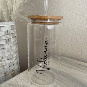 May include: A clear glass water bottle with a bamboo lid and a black straw. The bottle has the name "Vrixiana" written on it with the words "Wife, Mom, CEO" underneath.