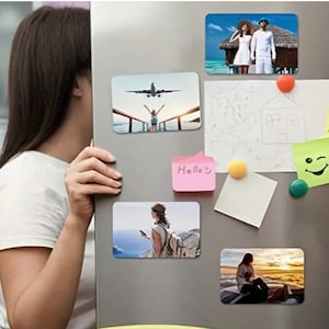 May include: A white refrigerator with several magnets attached to it. The magnets include photos of people, a drawing of a house, and a smiley face. There is also a sticky note with the text "Hello" and another sticky note with the text "Good morning".