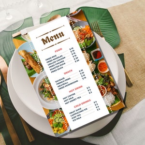 以下が含まれることがあります： 茶色の枠と茶色のフォントで「Menu」と書かれた白いメニュー。メニューは、ユーロ建ての価格で、食べ物と飲み物の項目をリストアップしています。メニューは、緑色のプレースマットと白いテーブルクロスのあるテーブルの上に置かれています。