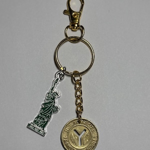 May include: Gold keychain with a green Statue of Liberty charm and a gold coin with the text "NEW YORK CITY TRANSIT AUTHORITY" and a stylized "NYC" logo.