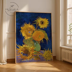 Può includere: Stampa incorniciata del dipinto "Girasoli" di Van Gogh. L'opera presenta vibranti girasoli gialli in un vaso verde su uno sfondo blu intenso. La stampa è in una cornice dorata ed è esposta in una stanza con luce naturale.