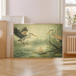 May include: A framed print featuring two herons in a wetland scene. One heron is in flight, wings spread, while the other perches on a branch. The artwork has a vintage aesthetic, with muted greens, blues, and browns.