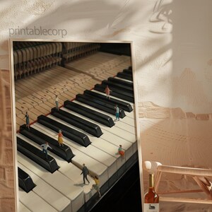 May include: A framed print featuring a detailed image of a piano keyboard with miniature figures walking on the keys. The print has a light-colored frame and is set against a neutral background. A bottle of wine sits nearby.