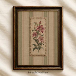 May include: A rectangular wall art print in a dark brown frame featuring a vertical botanical illustration of pink lilies centered on a beige and green striped background. The floral artwork is enclosed in a decorative border with small red flowers.
