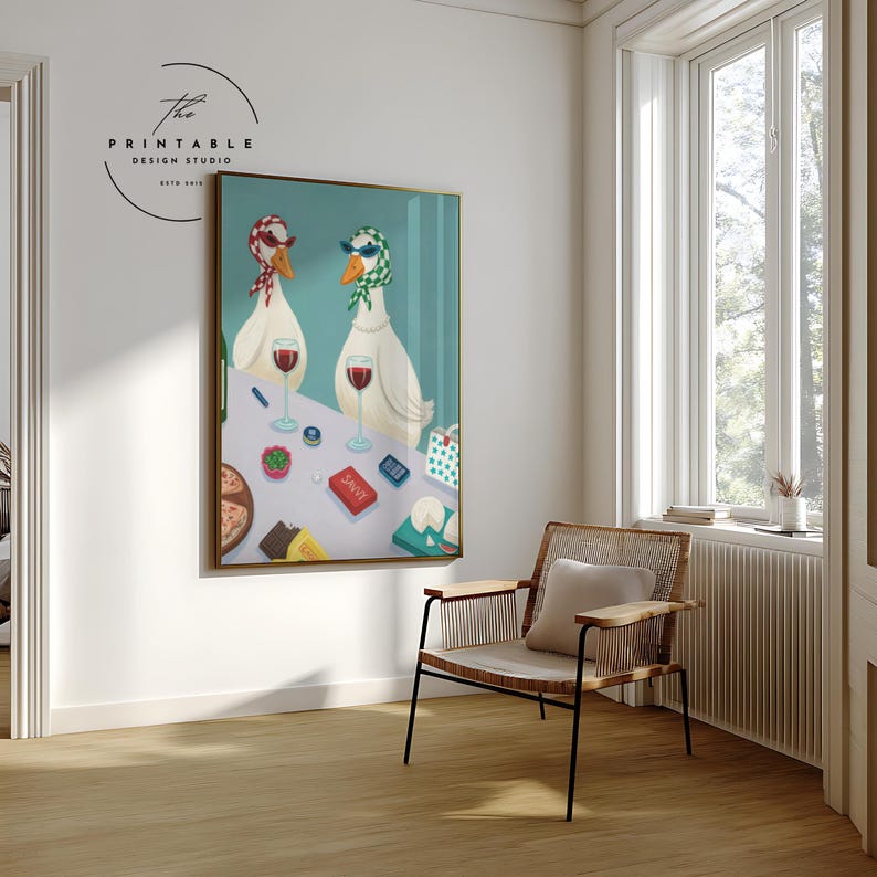 May include: A framed art print featuring two anthropomorphic geese wearing headscarves and sunglasses, enjoying wine at a table. The table is set with pizza, gifts, and other items. The artwork is displayed in a room with a chair and a window.