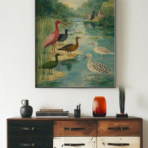 Puede incluir: Una impresi&oacute;n art&iacute;stica enmarcada que presenta una pintura a la acuarela de varias especies de aves en un entorno de humedal. La obra de arte incluye aves en tonos rosa, negro, verde y blanco, paradas en el agua. La impresi&oacute;n se exhibe sobre una c&oacute;moda de madera.