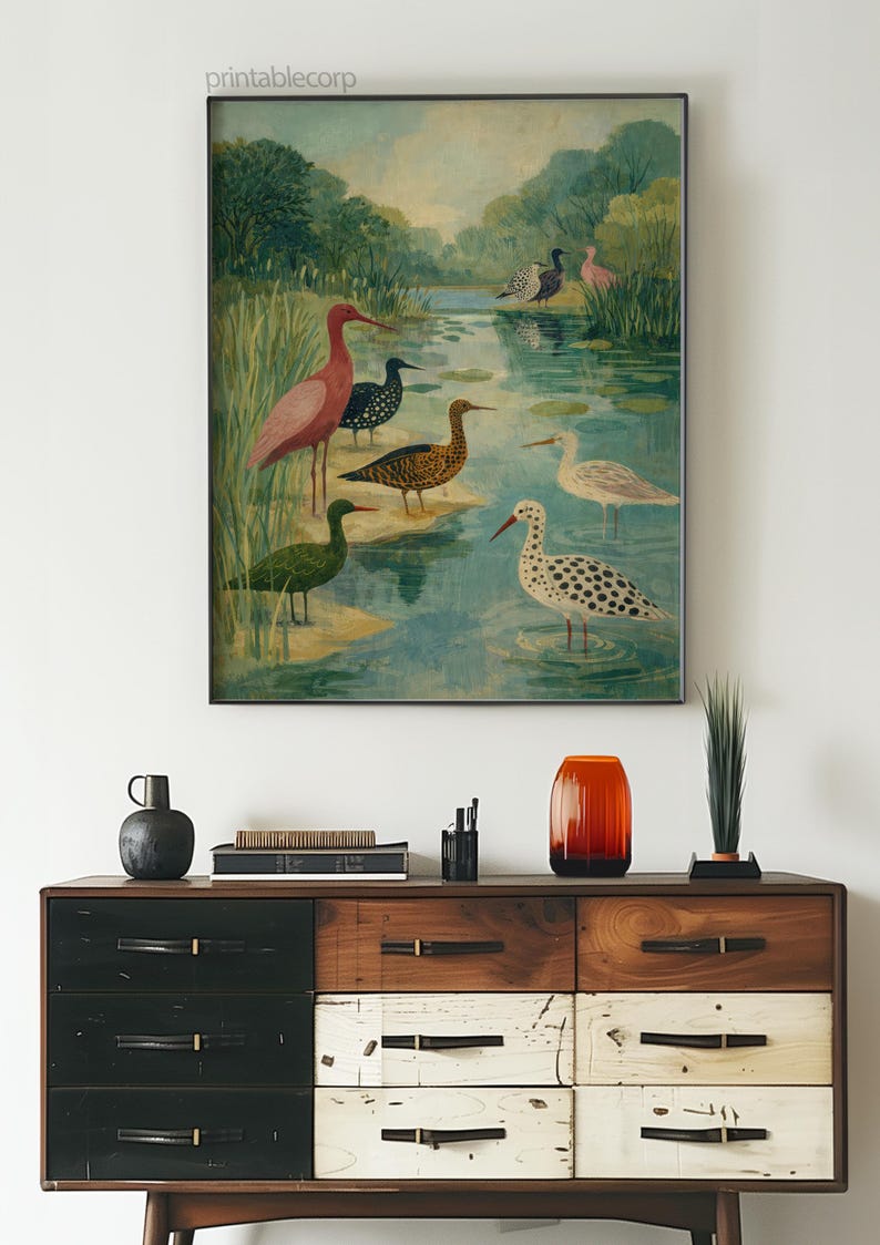 Puede incluir: Una impresi&oacute;n art&iacute;stica enmarcada que presenta una pintura a la acuarela de varias especies de aves en un entorno de humedal. La obra de arte incluye aves en tonos rosa, negro, verde y blanco, paradas en el agua. La impresi&oacute;n se exhibe sobre una c&oacute;moda de madera.