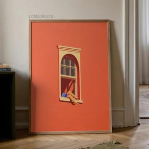 May include: A framed art print featuring a stylized illustration of a window on a coral-colored wall. The window has a white arched top and a person's legs are visible, with blue shorts. The print is displayed on a wooden floor.