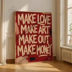 May include: A framed art print with the words "MAKE LOVE MAKE ART MAKE OUT MAKE MONEY" in white brushstrokes on a red background. The artwork has a vintage, hand-painted aesthetic.