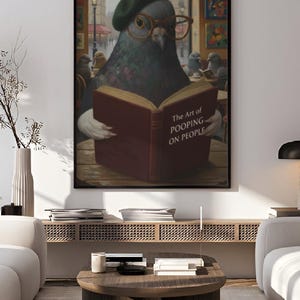 May include: A framed art print featuring a pigeon wearing a beret and glasses, reading a book titled "The Art of Pooping on People." The artwork has a humorous theme and is set in a cafe with other pigeons.