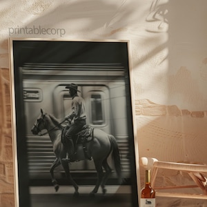 May include: Black and white framed print featuring a cowboy riding a horse past a speeding train. The image has a vintage aesthetic. A bottle of wine sits in front of the print. The text "printablecorp" is visible in the upper left corner.