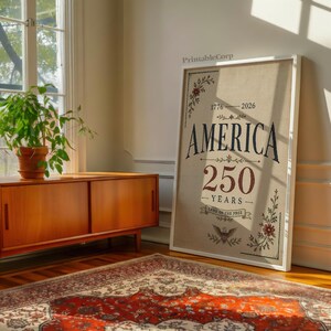 Pu&ograve; includere: Stampa su tela incorniciata con la scritta "AMERICA 250 YEARS" in blu navy e bordeaux. La stampa &egrave; decorata con elementi floreali e un'aquila. La cornice &egrave; bianca e la tela ha uno sfondo beige.