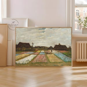 Op de afbeelding: Een ingelijste print van een kleurrijk tulpenveld met een boerderij op de achtergrond. Het kunstwerk toont een verscheidenheid aan kleuren, waaronder roze, geel, wit en blauw. De lucht is bewolkt en de stijl is impressionistisch.
