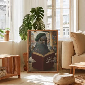May include: A framed art print featuring a pigeon wearing a beret and glasses, reading a book titled "The Art of Pooping on People." The artwork has a humorous theme and is set in a cafe.
