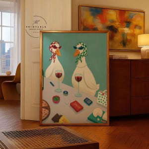 May include: A framed art print featuring two anthropomorphic geese wearing sunglasses and scarves, enjoying wine. The artwork includes a table with snacks and the word "SAVVY" on a box. The background is a light teal color.