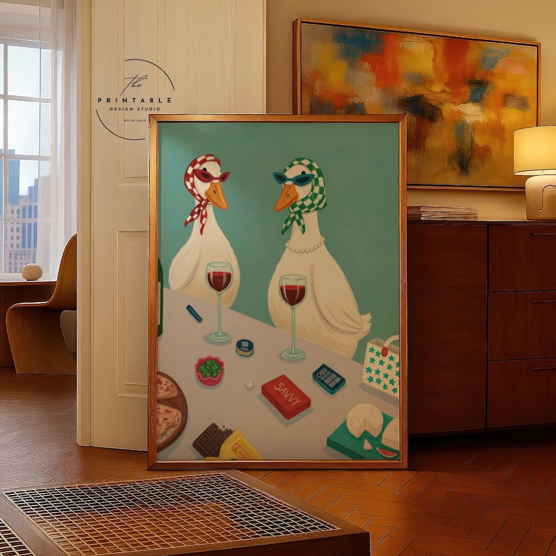 May include: A framed art print featuring two anthropomorphic geese wearing sunglasses and scarves, enjoying wine. The artwork includes a table with snacks and the word "SAVVY" on a box. The background is a light teal color.