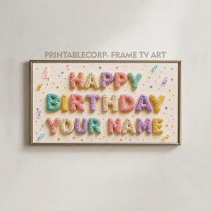 May include: A framed print with the words "HAPPY BIRTHDAY YOUR NAME" in colorful, textured letters. The letters are in shades of blue, pink, yellow, and purple, with confetti and stars scattered around. The frame is gold.