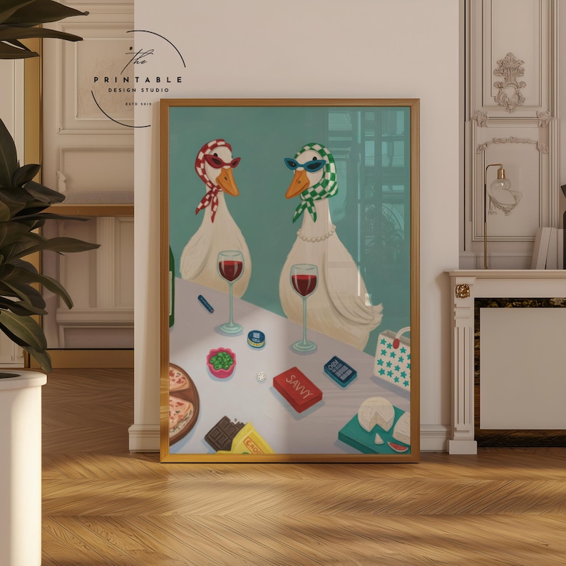 May include: A framed art print featuring two geese wearing sunglasses and scarves, enjoying wine and snacks. The artwork includes a table with pizza, cheese, and a box labeled "SAVVY". The background is a light teal color.