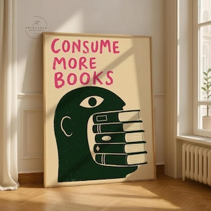 May include: A rectangular wall art print on a cream background featuring the pink text "CONSUME MORE BOOKS" above a dark green silhouette of a human head with an open mouth containing a stack of five books with visible white page edges.