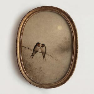 Puede incluir: Obra de arte enmarcada ovalada con dos pájaros posados en una rama. Las aves tienen marcas rojas y marrones. La obra de arte tiene un tono sepia con un marco dorado. El fondo representa un cielo brumoso con luna llena.